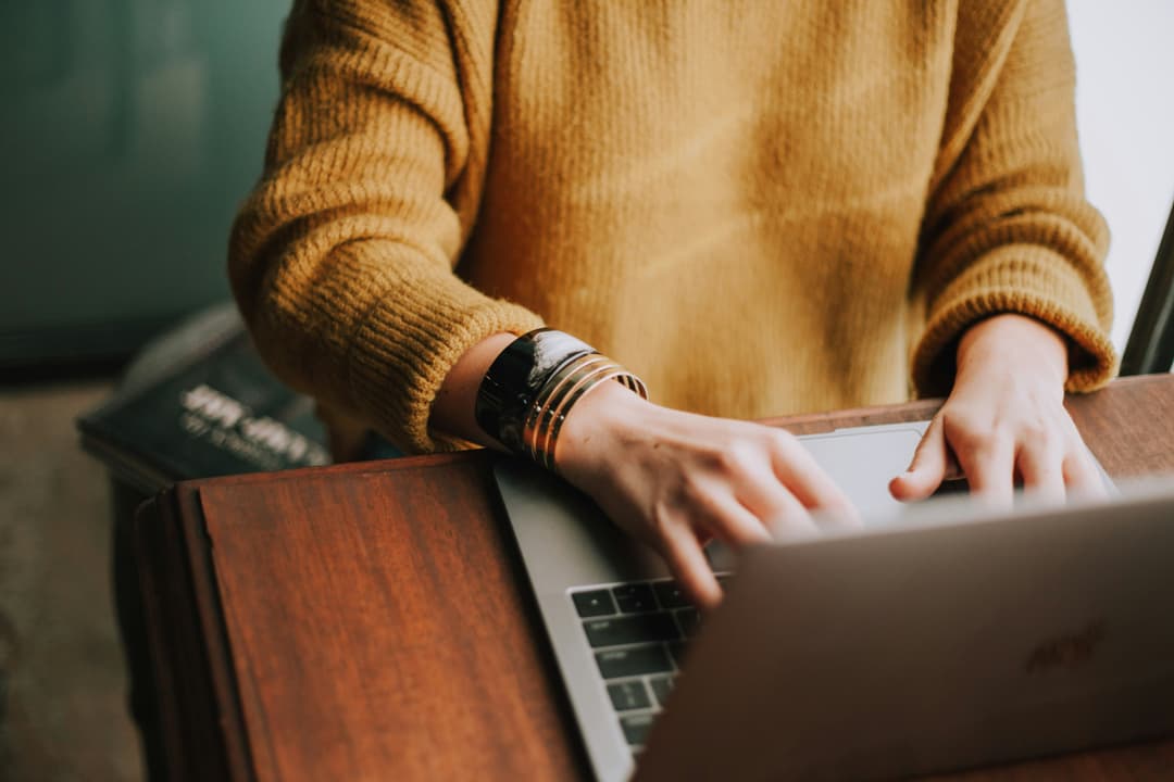 Human with yellow sweater typing on a laptop